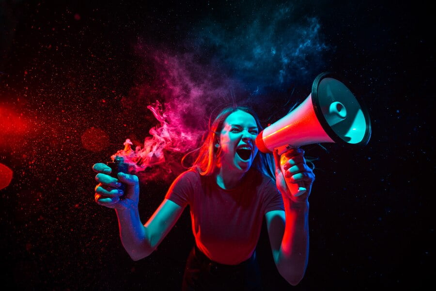 Gritando com megafone. jovem mulher com fumaça e luz de néon em fundo preto. altamente tenso, grande angular, visão de olho de peixe.