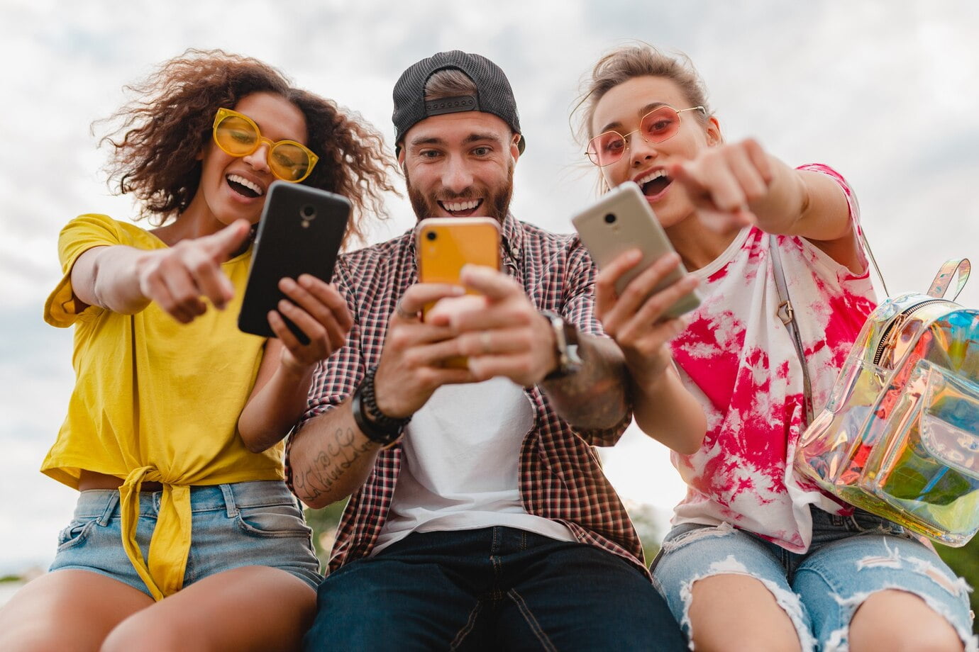 Jovem e feliz companhia de amigos sorridentes sentados no parque usando smartphones