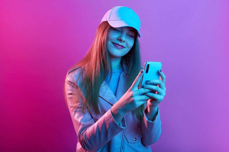 Retrato de uma jovem e bela modelo elegante usando couro padeiro e boné de beisebol, segurando o telefone inteligente nas mãos