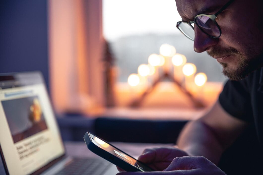 Como Melhorar a Experiência do Usuário em Seu Site? 2 Um homem com um smartphone sentado na frente de um laptop tarde da noite