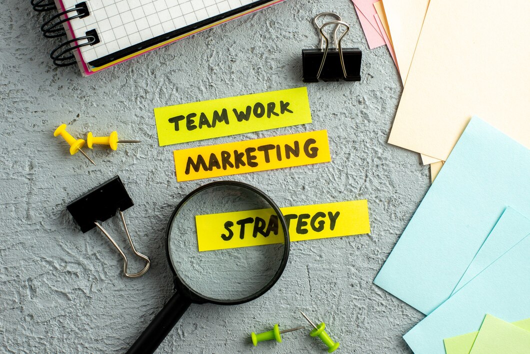 close up vista de envelopes coloridos escritos de estratégia de marketing trabalho em equipe no caderno espiral de lupa sobre fundo de areia cinza