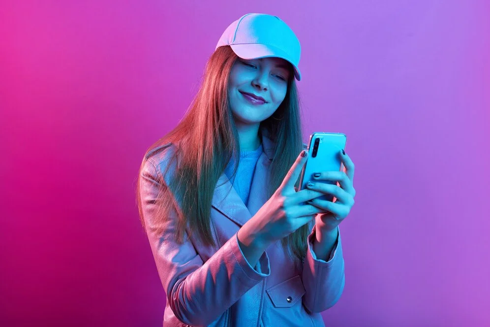Por que os mais jovens preferem o TikTok como ferramenta de busca ao Google? Retrato de uma jovem e bela modelo elegante usando couro padeiro e boné de beisebol, segurando o telefone inteligente nas mãos