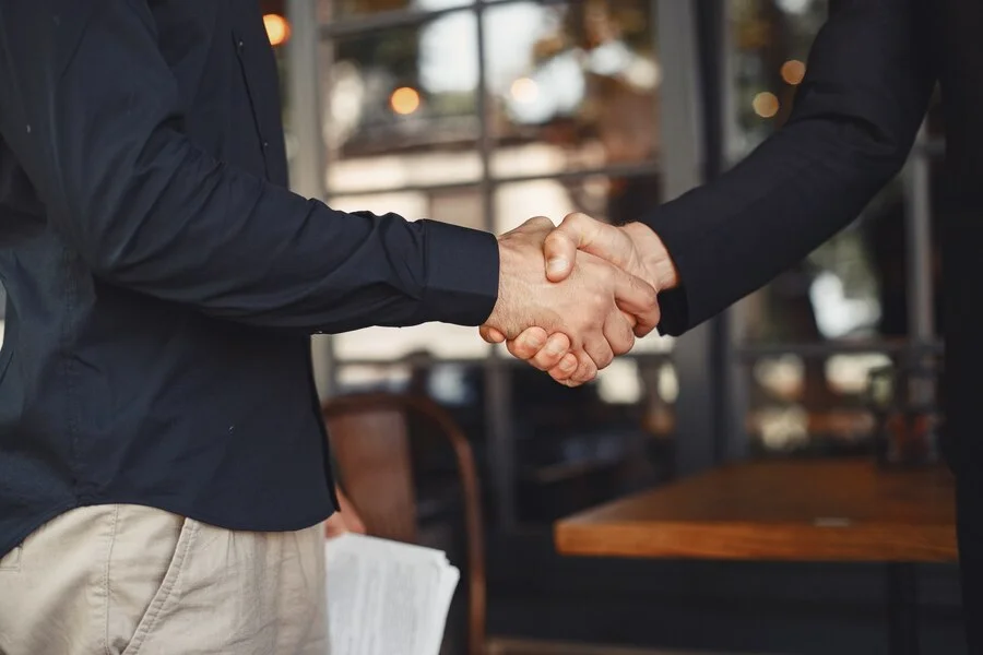 Como Escolher a Melhor Assessoria de Marketing? Homens apertam as mãos. Anexo de um acordo comercial. Entendimento entre parceiros de negócios.
