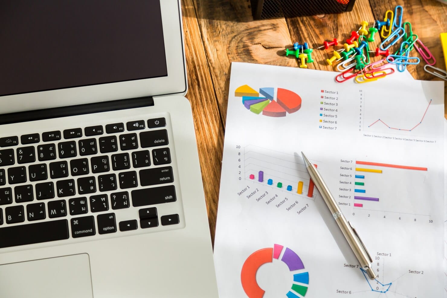 Laptop com gráficos de pizza ao lado dele e uma caneta
